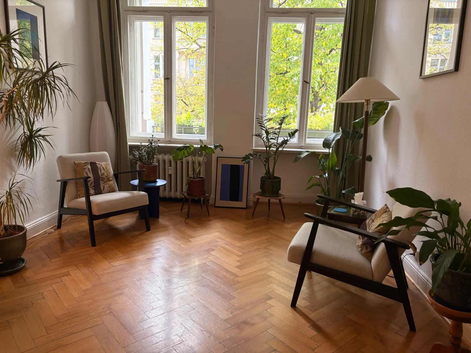 Blick in den Praxisraum mit zwei Sesseln, Pflanzen und großen Fenstern